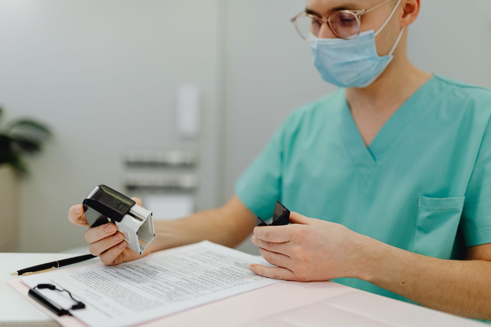 A clinician in scrubs completing and stamping a patient record at a desk, the administrative side of arranging care.