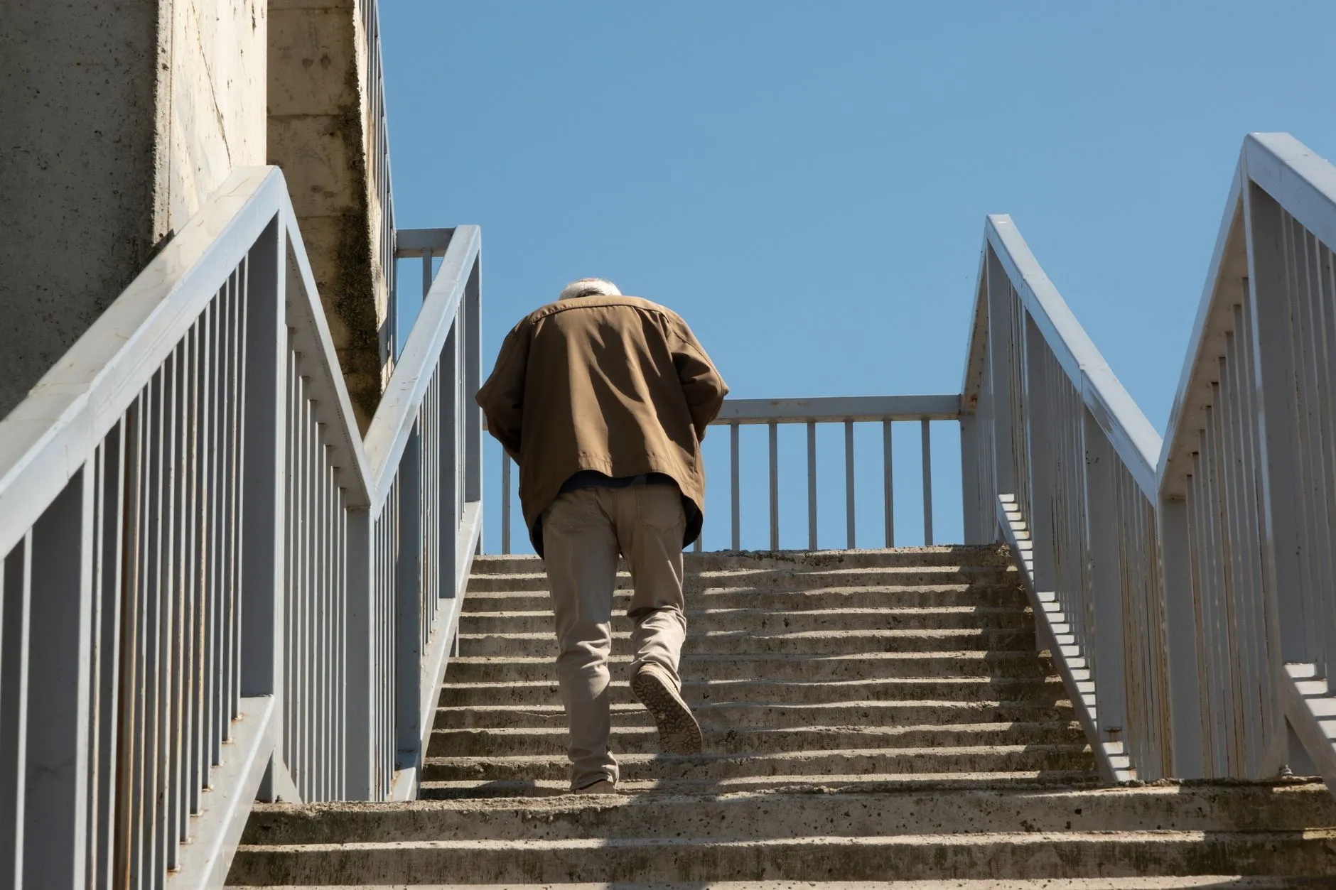 Older man climbing a long outdoor staircase while holding the metal railing